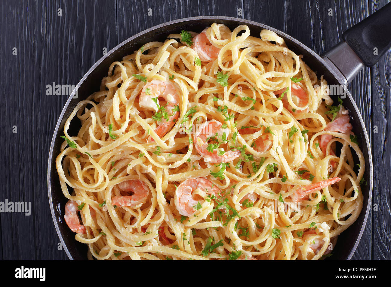 delicious one pot dinner - Creamy Shrimp Alfredo pasta sprinkled with finely chopped parsley in skillet on black wooden table, view from above Stock Photo