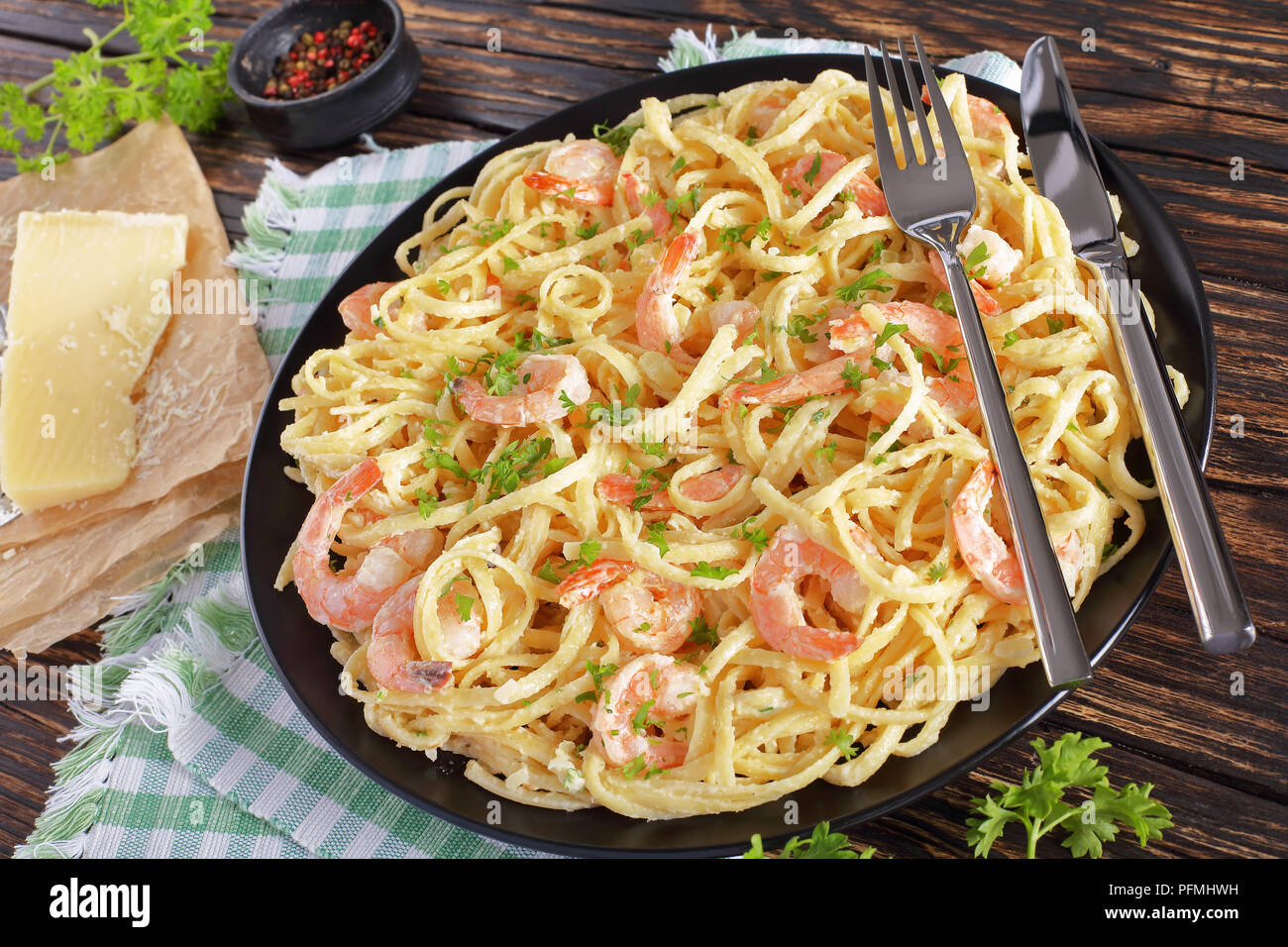 close-up of portion of Creamy Parmesan Shrimp pasta sprinkled with finely chopped parsley on black plate on wooden rustic table. piece of parmesan and Stock Photo
