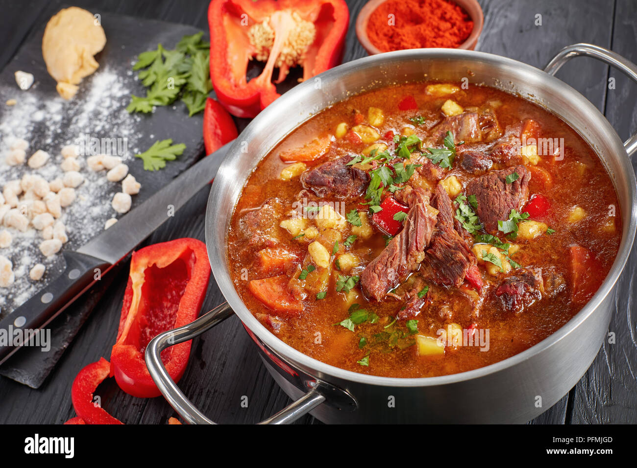 close-up of  hot beef hungarian goulash  or bograch soup with paprika, small egg pasta, vegetables and spices in a pot. ingredients and soup ladle on  Stock Photo