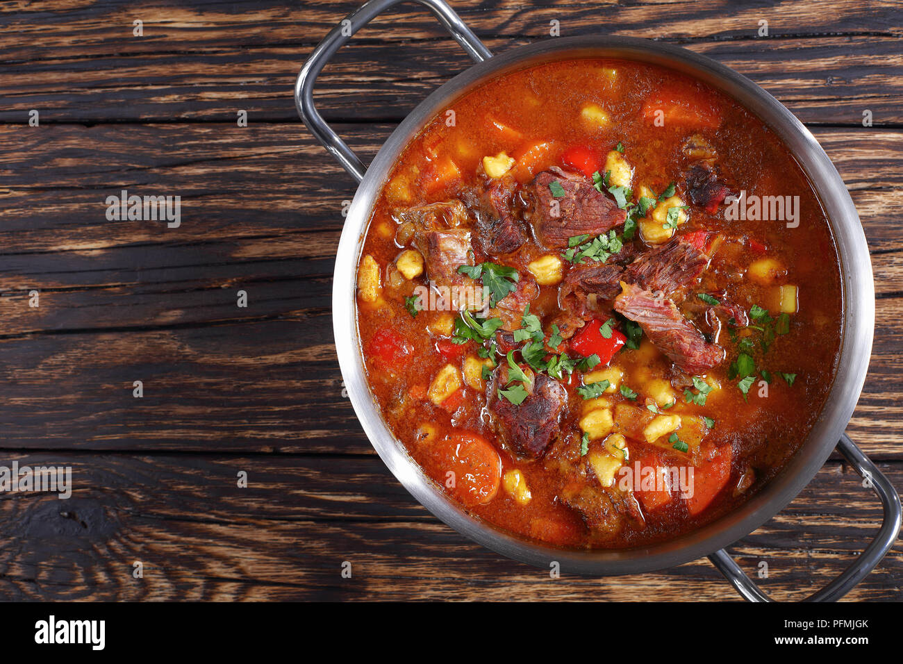 hot beef hungarian goulash or bograch soup with paprika, small egg pasta, vegetables and spices in a pot on wooden table, classic recipe, view from ab Stock Photo