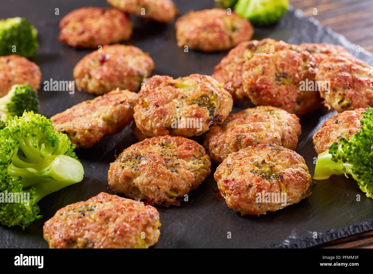 delicious baked meat broccoli patties with grated cheese, and spices on black slate tray on wooden table, healthy low calories recipe, view from above Stock Photo