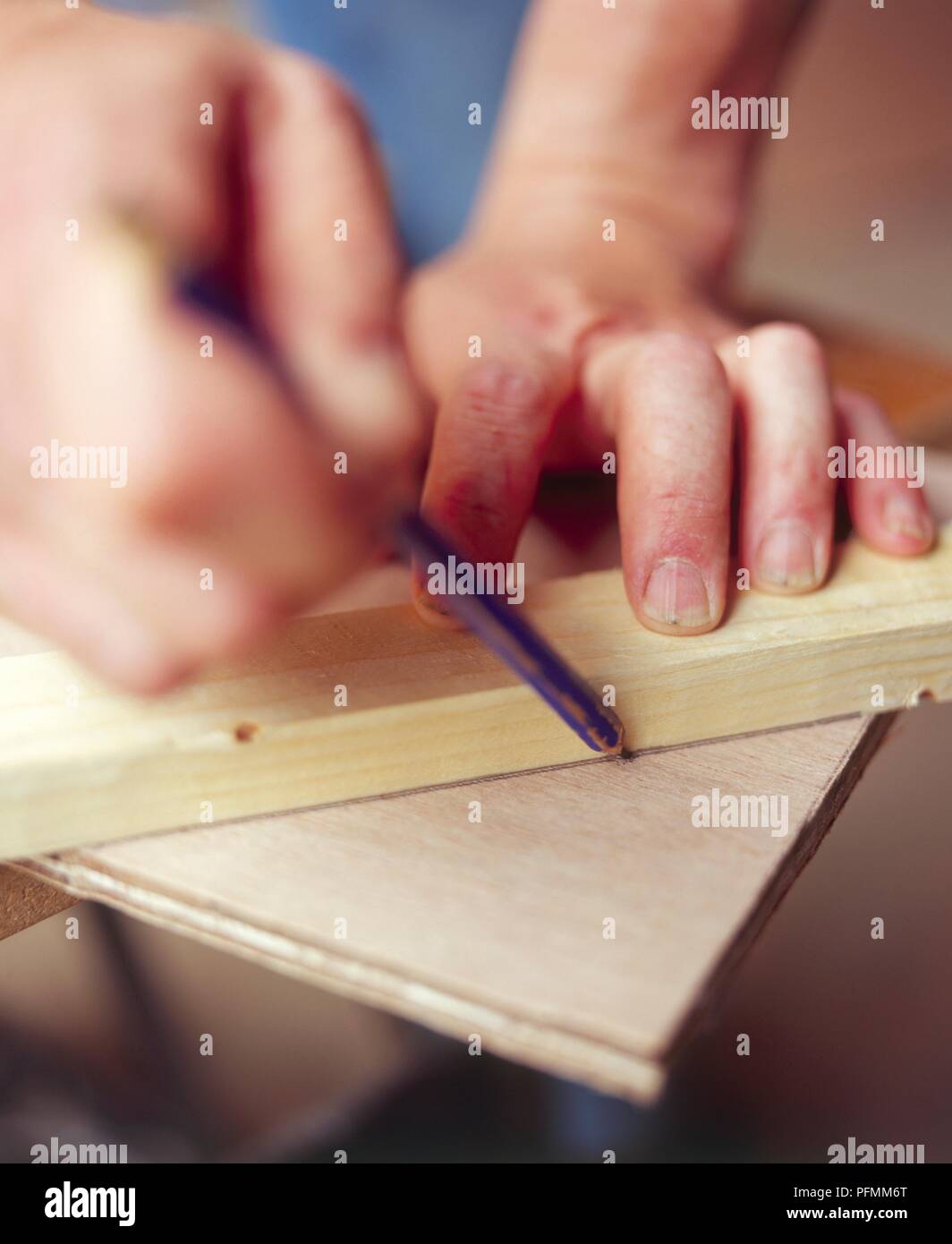 Using a pencil and a piece of wood to mark a diagonal across the corner of a piece of plywood, close-up Stock Photo