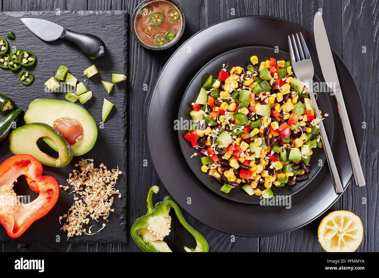 mexican style salad with avocado, black beans, corn kernels, buckwheat sprouts, diced pepper served on black plates with ingredients on stone board an Stock Photo