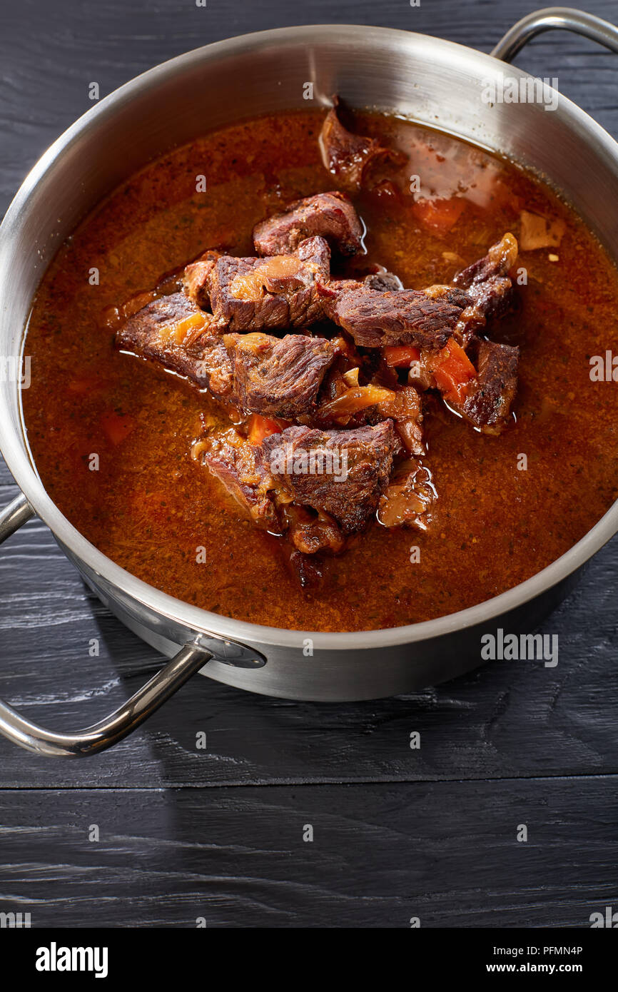 homemade hot Czech beef goulash in a stainless pan on black wooden table, vertical view from above Stock Photo