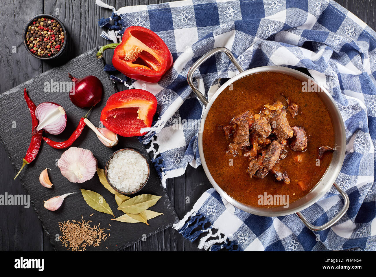 delicious homemade hot traditional Czech beef goulash in a stainless pan on black wooden table with ingredients on cutting board, view from above Stock Photo