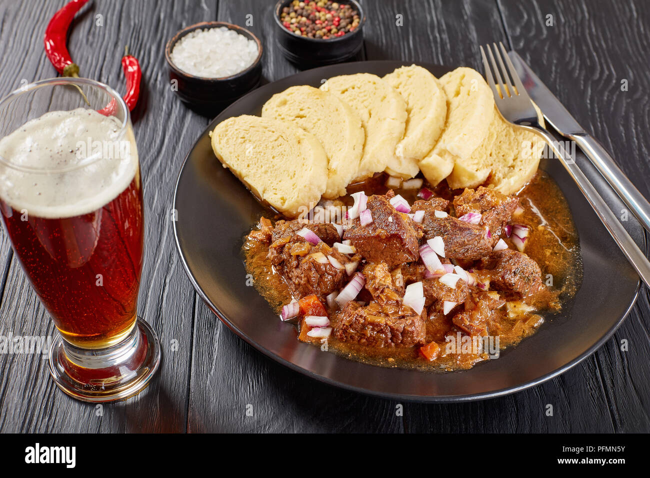 delicious homemade hot traditional Czech beef goulash served with steamed czech dumplings or knedliky on black plate on wooden table with glass of bee Stock Photo