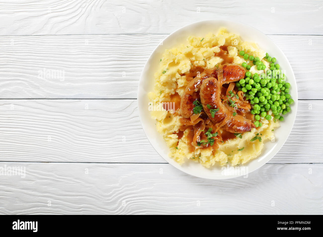 delicious Bangers and Mash - juicy fried hot sausages with brown crust in thick onion gravy with mashed potatoes and green peas, classic recipe, view Stock Photo