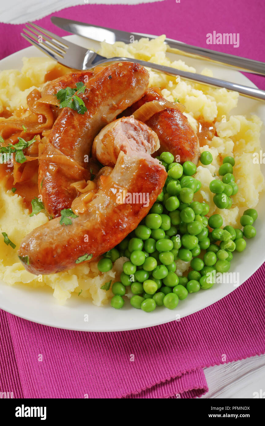delicious Bangers and Mash - juicy fried sausages drowning in loads of onion gravy, with creamy mashed potatoes and green peas, classic recipe, verti Stock Photo