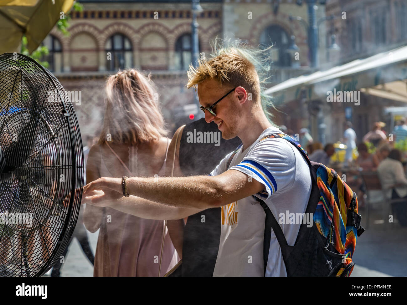 BUDAPEST,HUNGARY-AUGUST 09,2018:People alleviate the summer heat wave in front of the water spraying fan at the street of downtown. Stock Photo