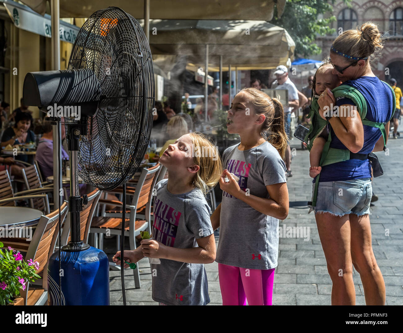 BUDAPEST,HUNGARY-AUGUST 09,2018:People alleviate the summer heat wave in front of the water spraying fan at the street of downtown. Stock Photo