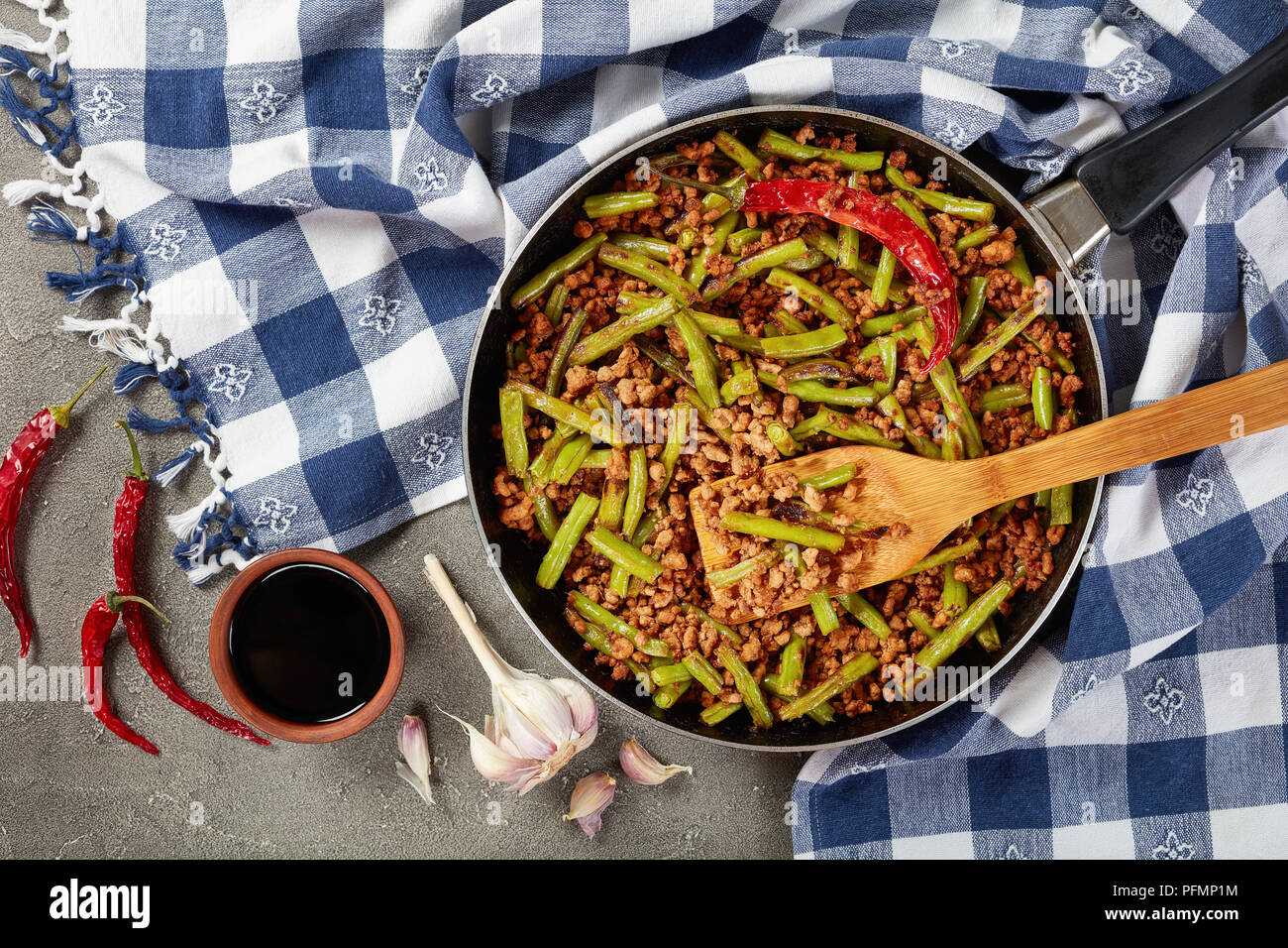 Szechuan Pork Stir Fry with Green Beans in a skillet on concrete table with soy sauce and dried chili peppers,  view from above, close up, flat lay Stock Photo