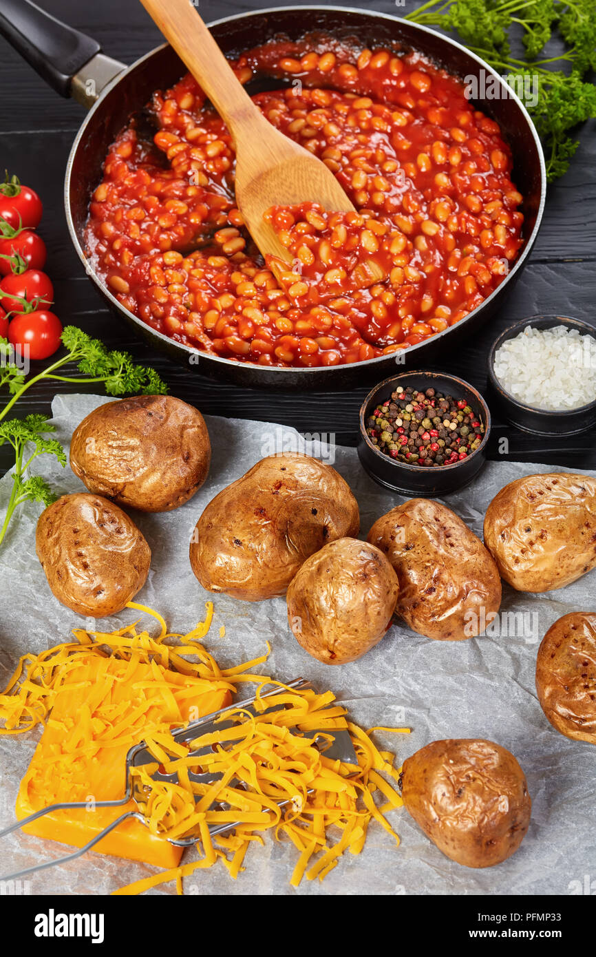 baked potato or jacket potatoes with golden brown crispy skin on a paper with cheddar cheese. baked bean with tomato sauce in a skillet at background, Stock Photo