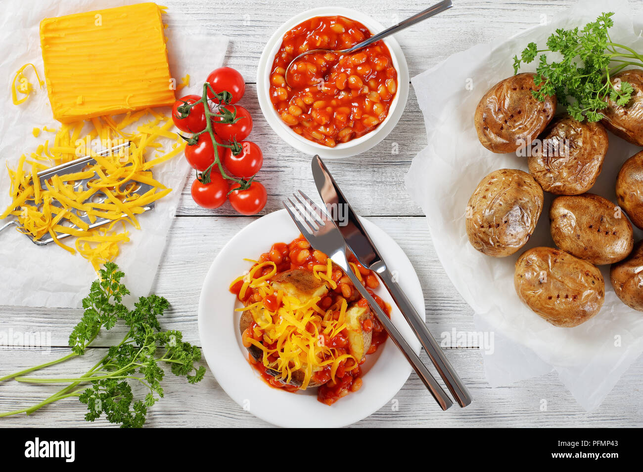 Baked Jacket Potato With Baked Beans And grated Cheese filling on white plate on wooden table with ingredients at background, view from above Stock Photo