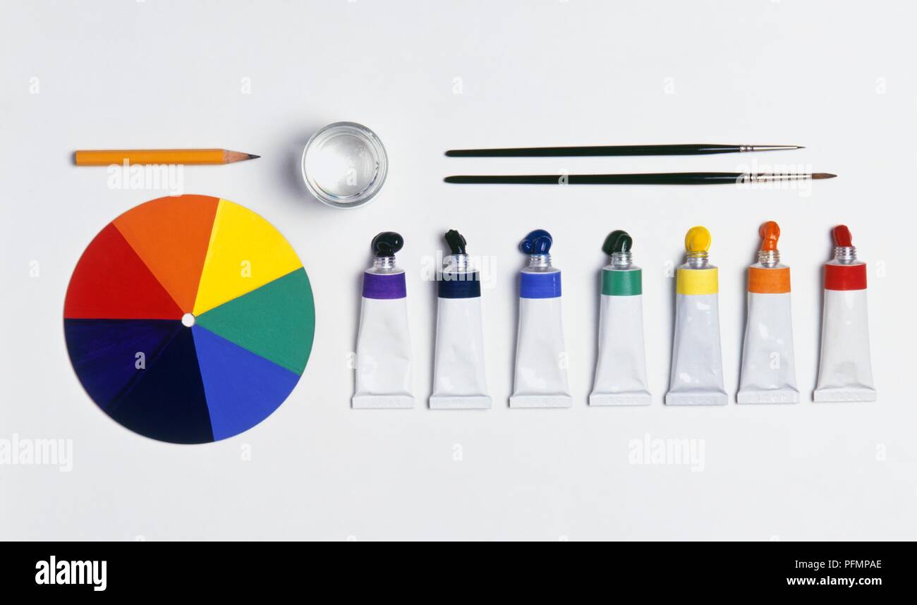 Open tubes of paint, paint brushes, pencil, glass of water and colour wheel Stock Photo