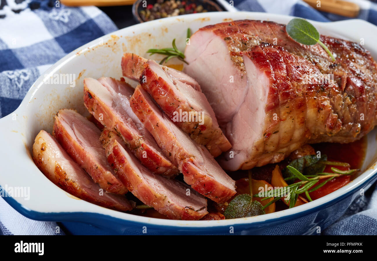 delicious juicy roast piece of pork meat cut in slices in a baking dish on wooden table with kitchen towel at background, view from above, close-up Stock Photo