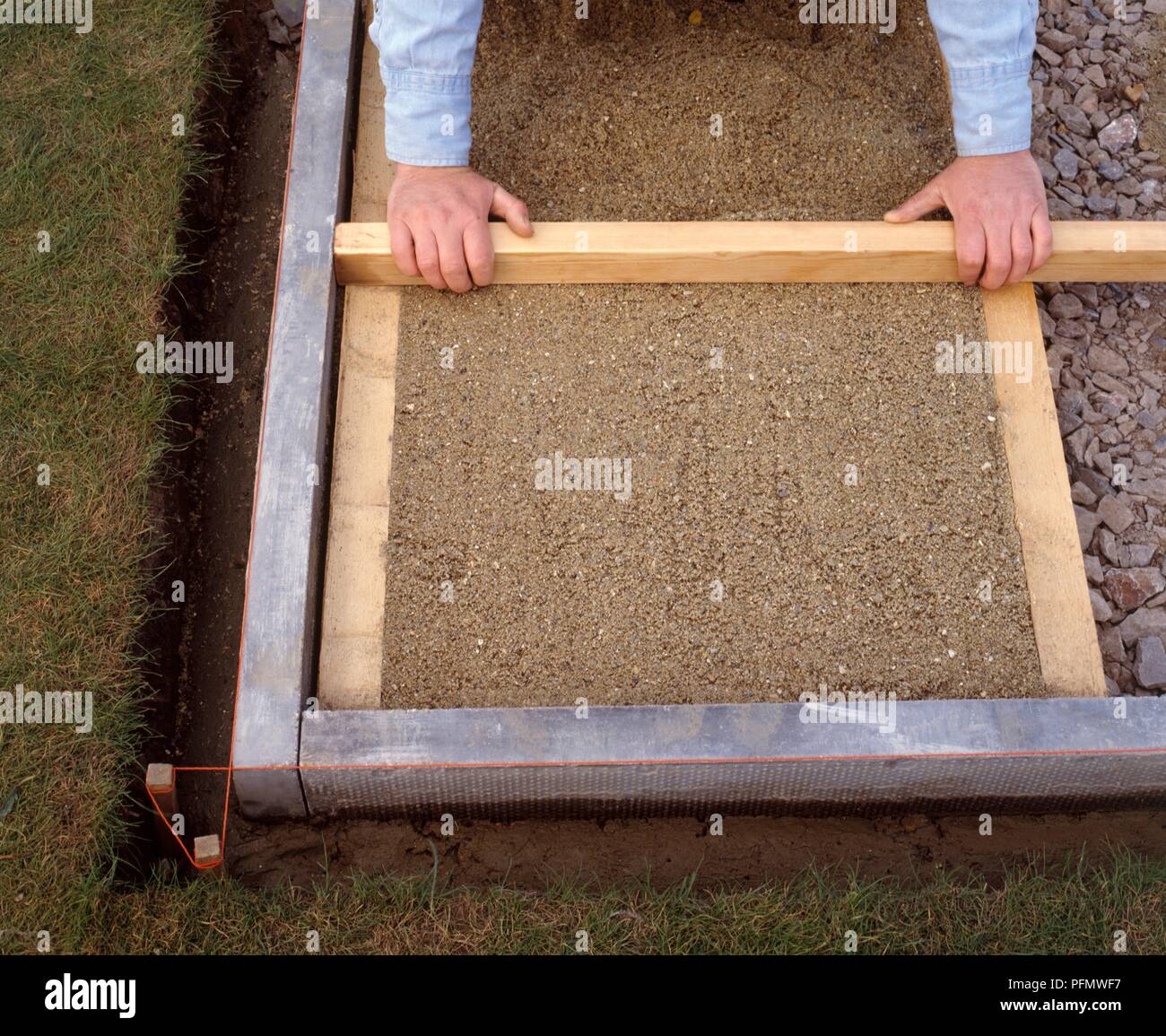 Laying a patio, levelling the sand to the tops of the battens with a length of wood, close-up Stock Photo