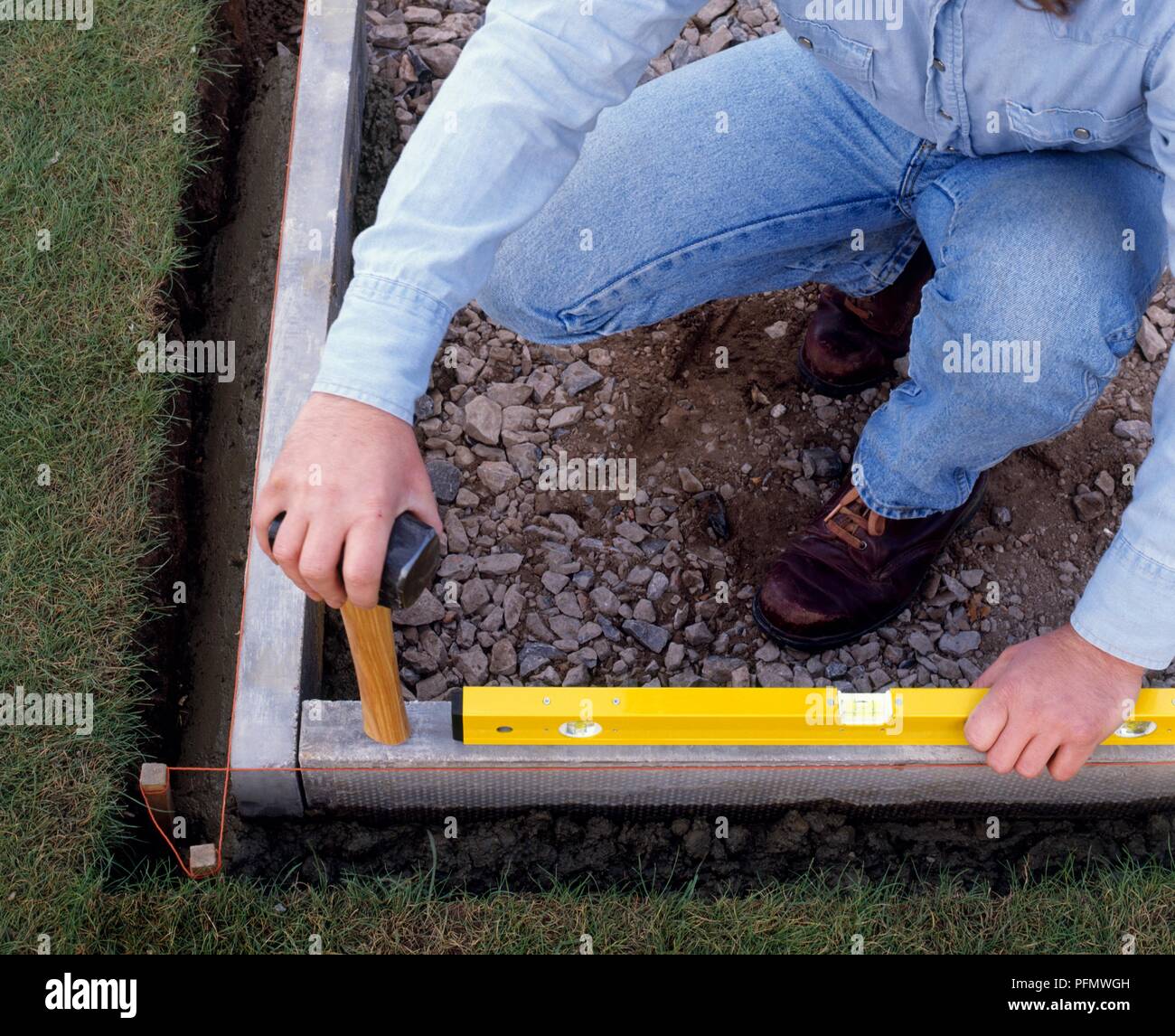 Laying a patio, using a spirit level and hammer to tap concrete edging level, close-up Stock Photo