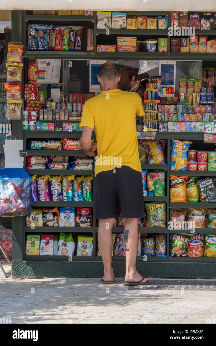 how much are cigarettes in corfu man standing at a kiosk selling sweets, cigarettes and confectionery in a  colourful display at a market stall in kerkyra on corfu in greece Stock  Photo