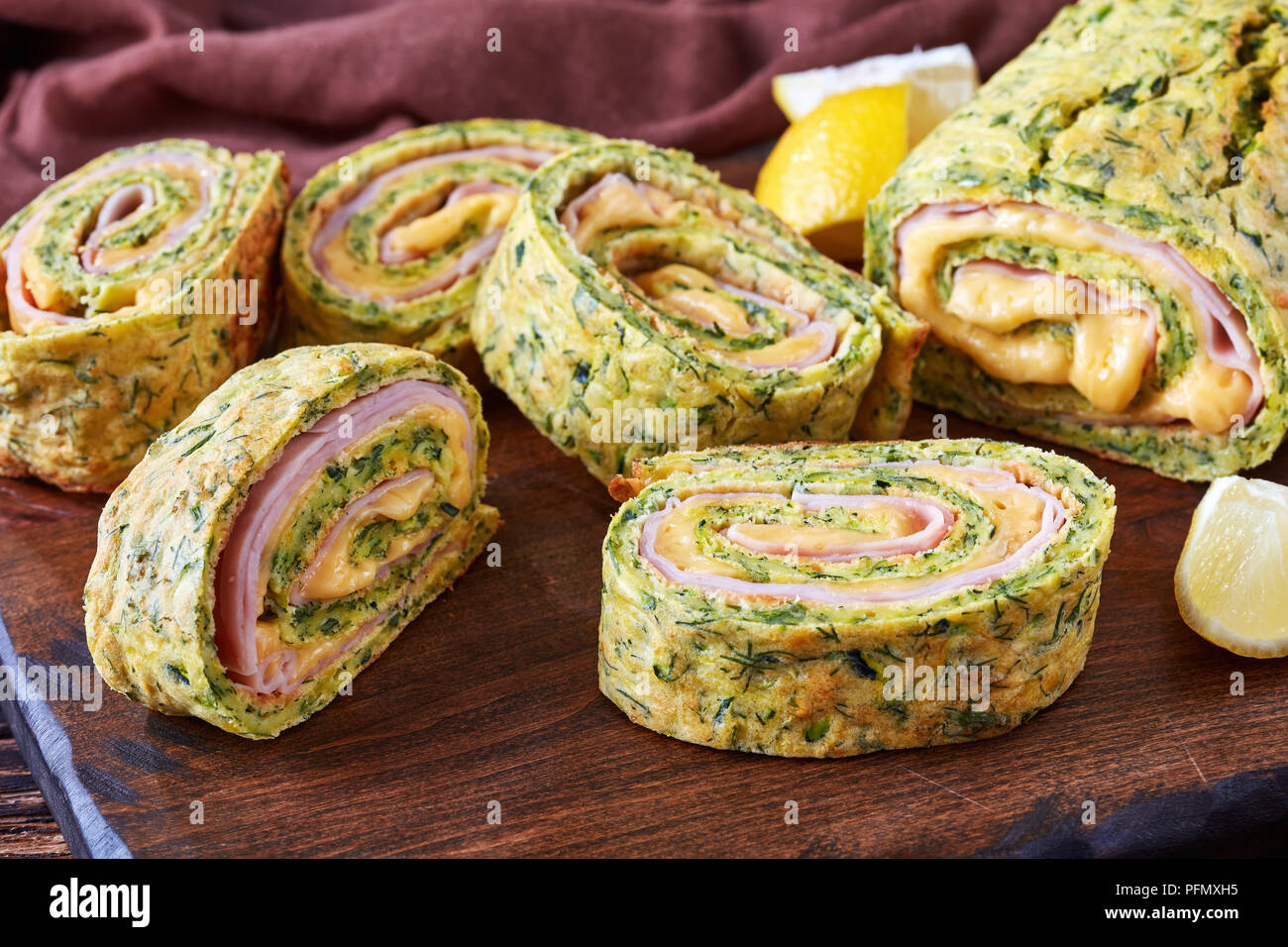 close-up of delicious zucchini roulade with melted cheese and boiled ham filling, cut in slices on a cutting board with savory yogurt sauce in a bowl  Stock Photo