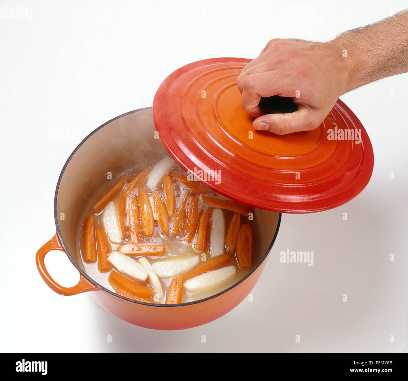 Hand lifting lid from pan of braised carrots and celeriac, close-up Stock Photo