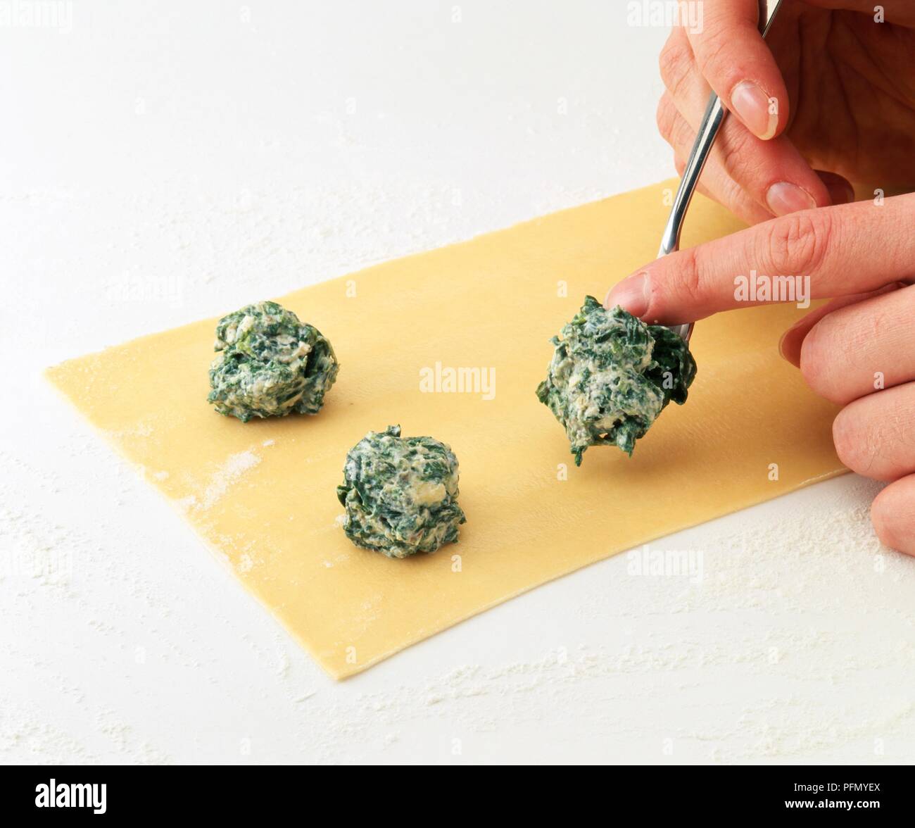 Hand placing spinach and ricotta filling onto pasta sheet, using a