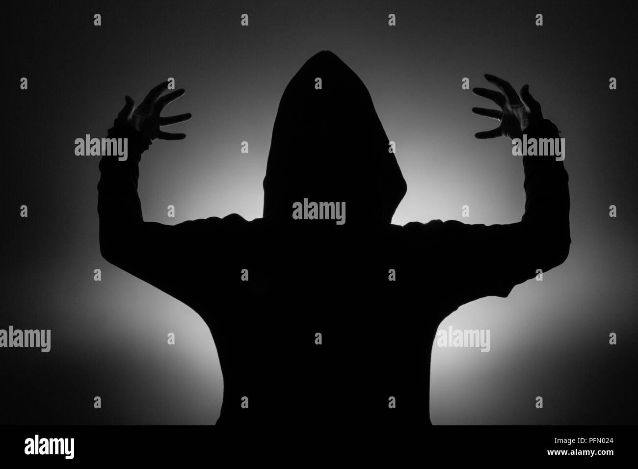 black and white photo: silhouette of a man in a hood holding a fantasy sword in Stock Photo