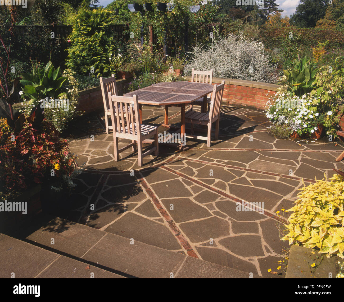 Wooden garden table and four chairs on a patio, floor made of asymmetric paving stones. Stock Photo