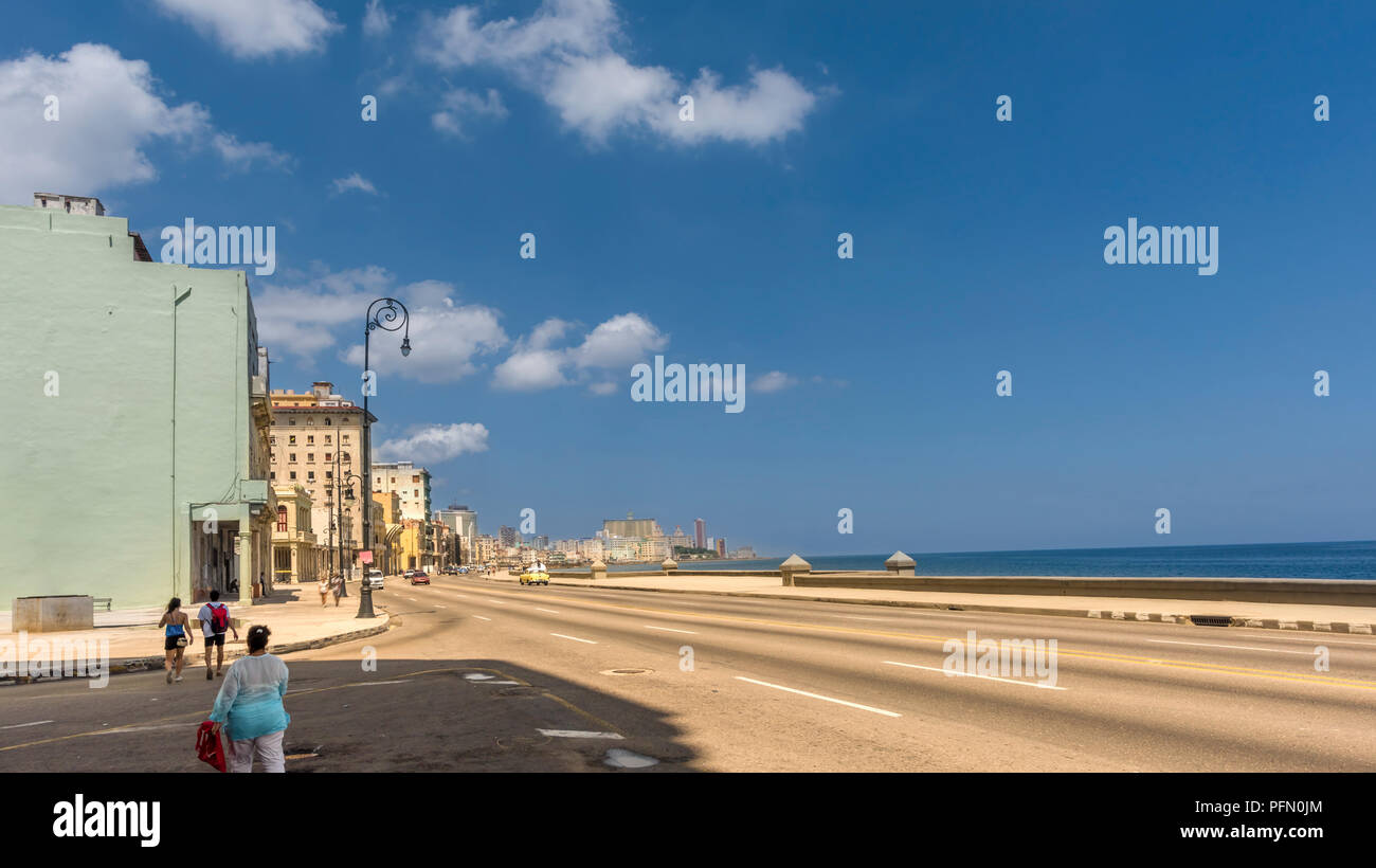 asphalt road on the embankment of an old tropical city, multi-story buildings, ocean, sky with clouds, cars, people walking along the street Stock Photo