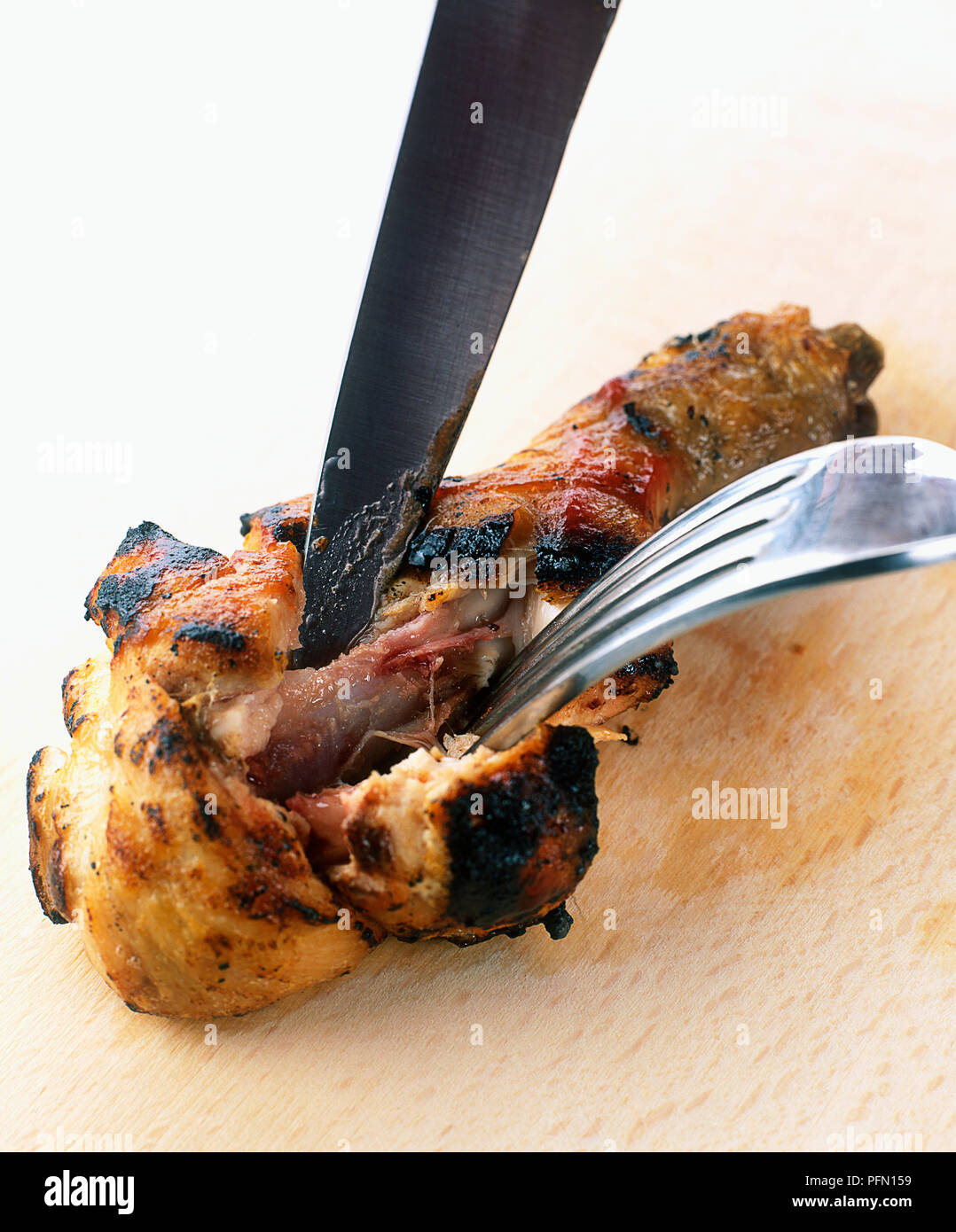 Cutting into chicken meat near bone, checking doneness Stock Photo