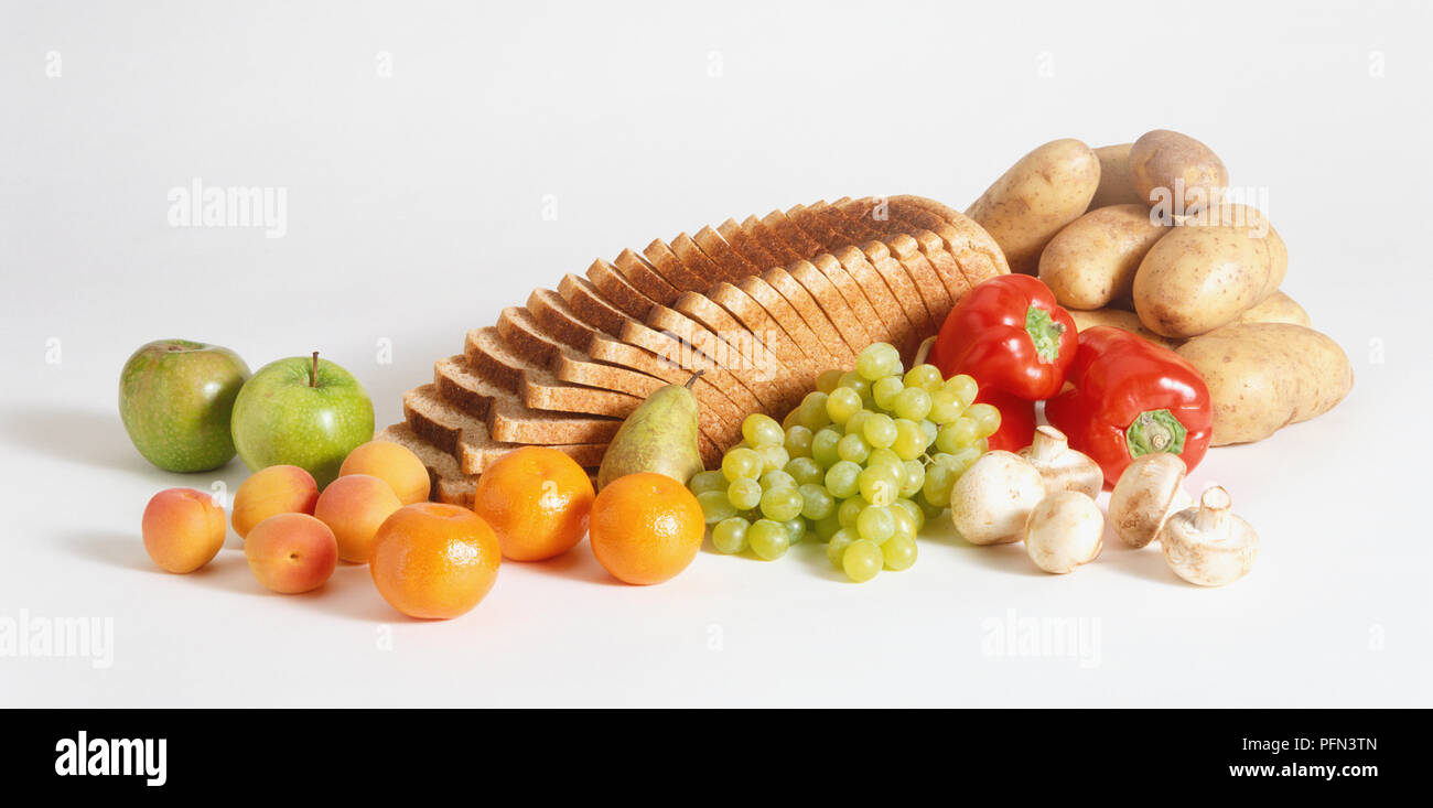 Selection of high-fibre foods, including slices of wholemeal bread, potatoes, red peppers, mushrooms, green grapes, pears, peaches and apples. Stock Photo
