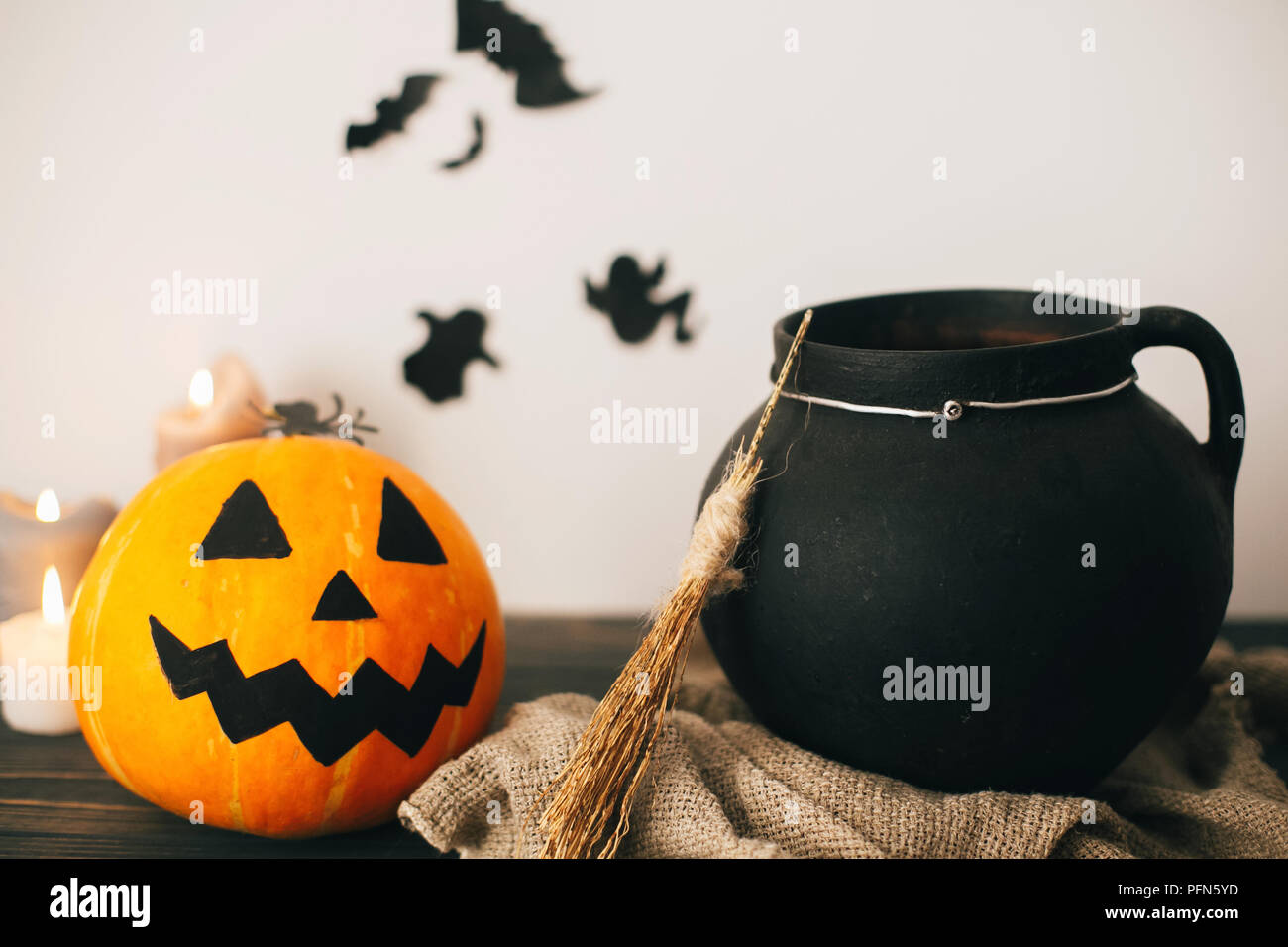 jack o lantern pumpkin with candles, bowl, witch broom and bats, ghosts on background in spooky room. Happy Halloween concept. fall halloween image. Stock Photo