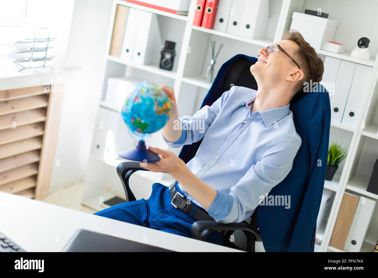 A young man sits in the office at the computer desk, closes his eyes ...