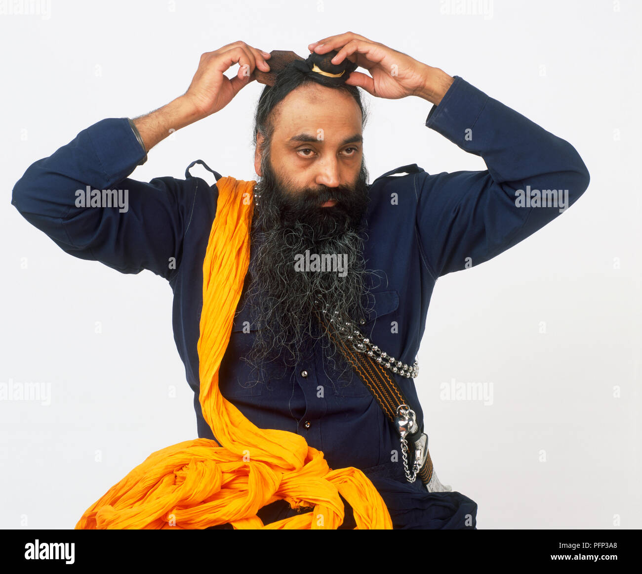 Man placing base cloth into position on his head, orange turban cloth hanging over his shoulder Stock Photo