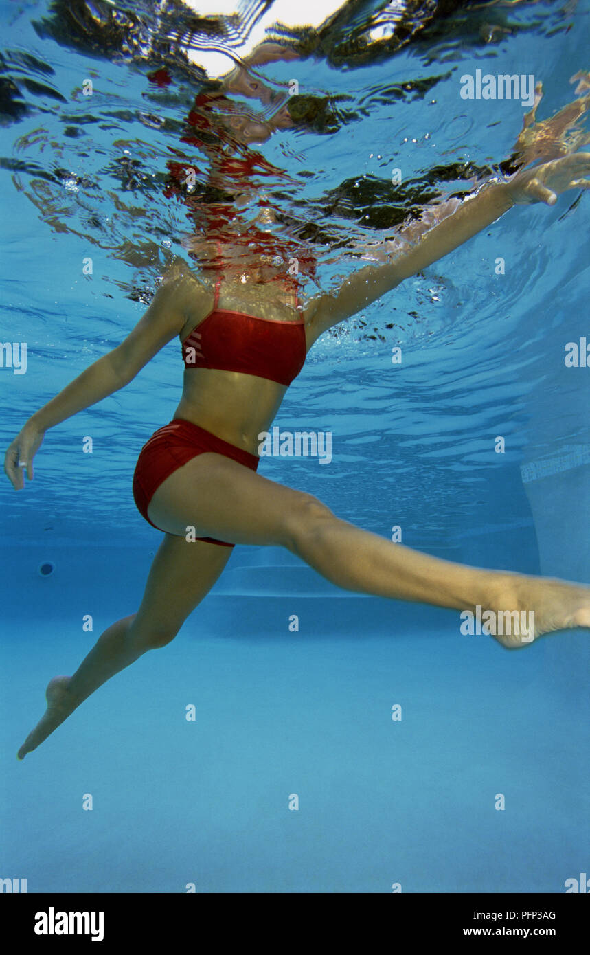 Woman in red swim wear, body submerged in water, with legs outstretched