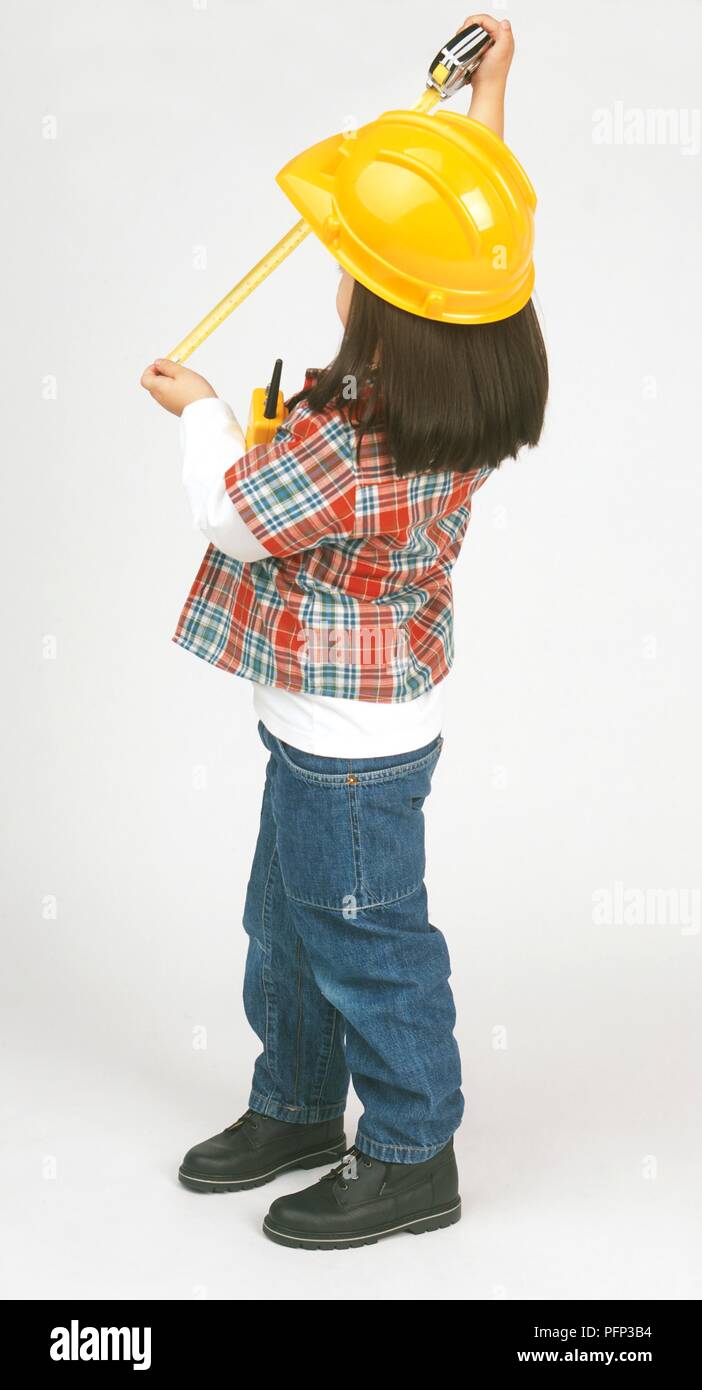 Girl dressed as a builder holding measuring tape, looking away Stock Photo
