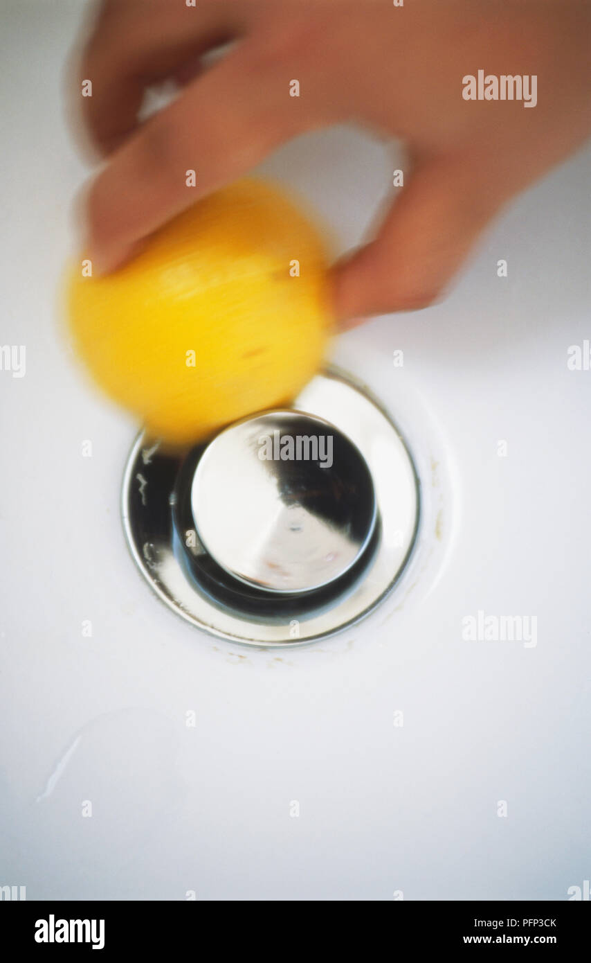 Holding halved lemon and rubbing lemon juice around drainage hole of bathroom sink, close-up, blurred motion Stock Photo