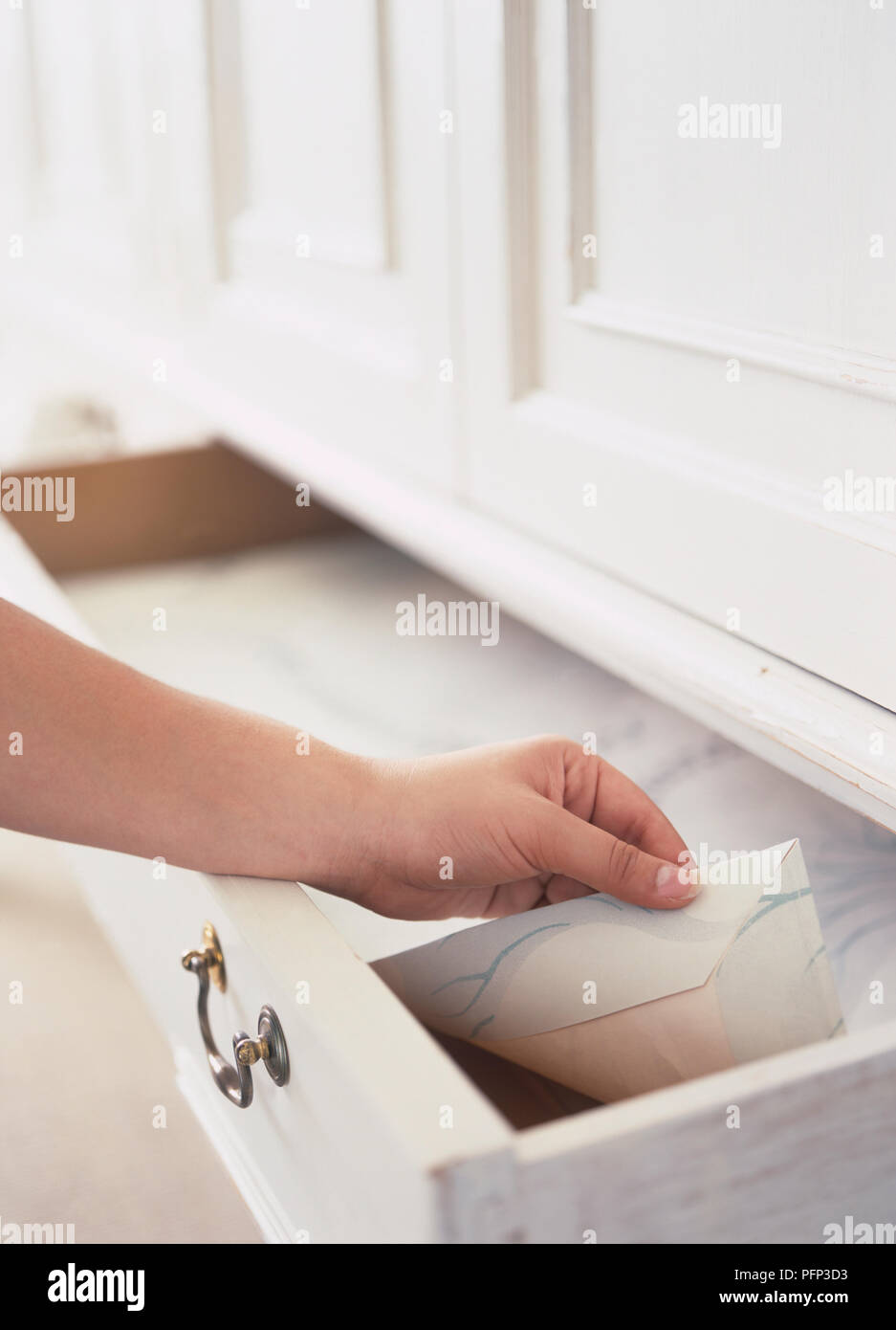 Woman's hand lifting drawer lining made from offcut of wallpaper, close
