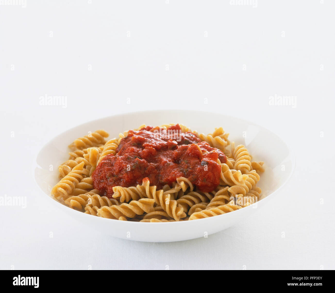 A white bowl filled with wholewheat pasta topped with rich tomato sauce