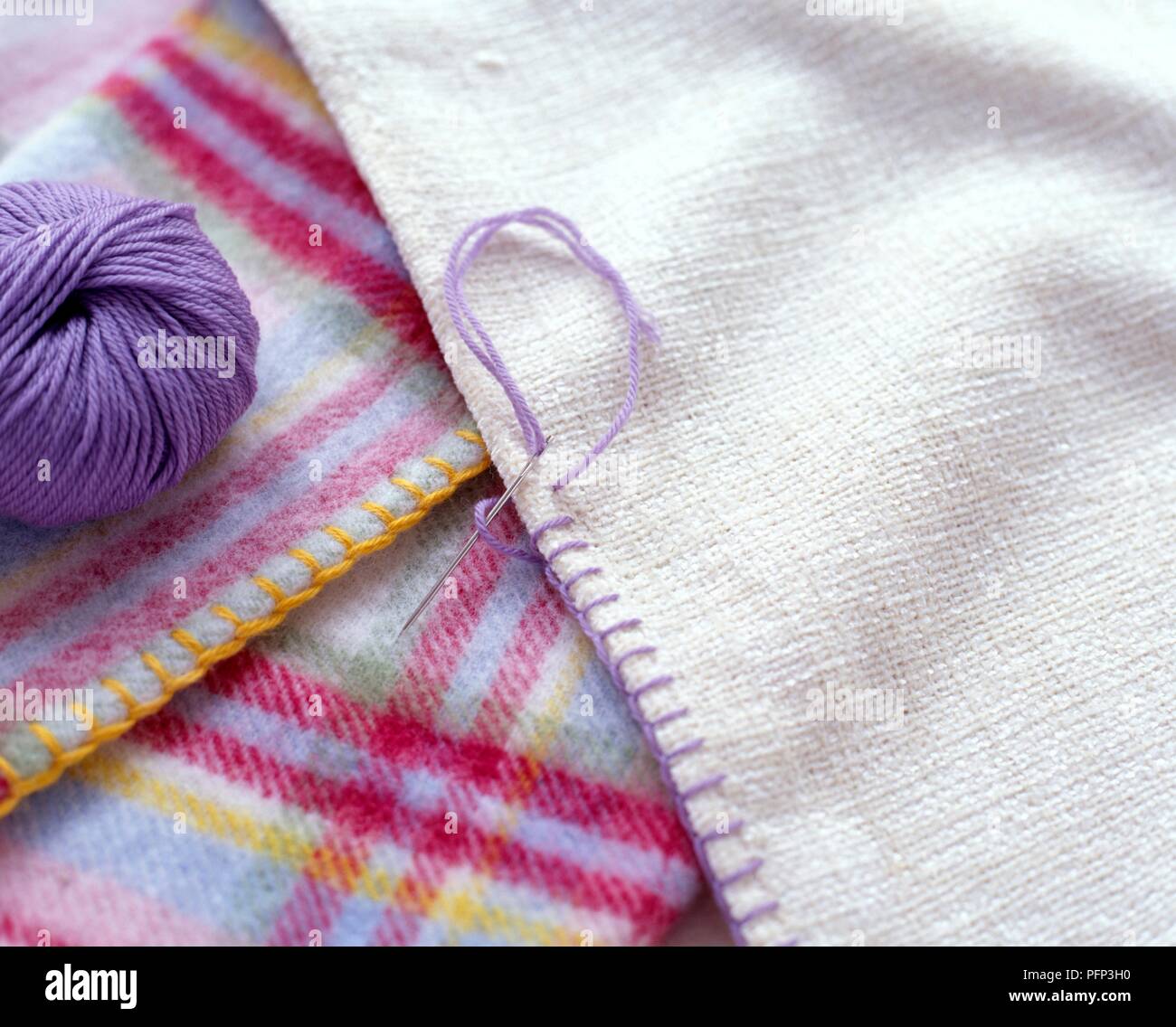 Blanket stitches decorating the edge of a fabric, ball of purple wool nearby Stock Photo