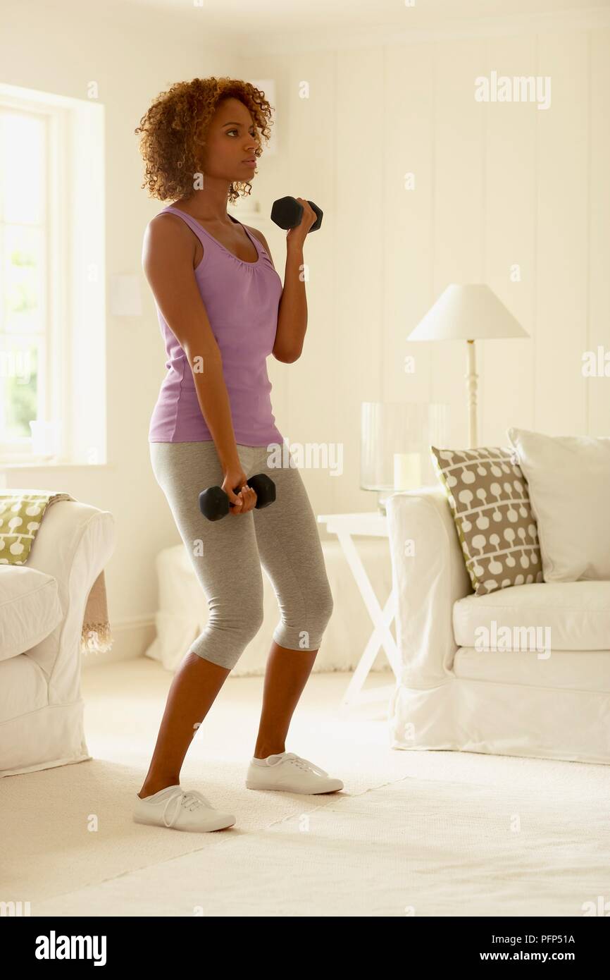 Woman in leggings and sleeveless top exercising with weights, standing, looking away Stock Photo