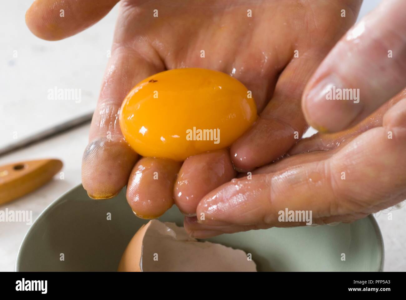 Hands holding egg yolk above bowl (mixing tempera paint), close-up Stock Photo