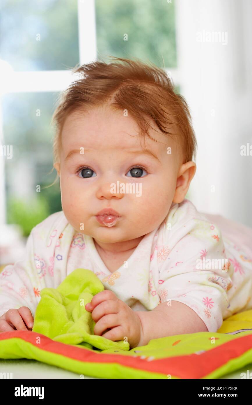 Baby girl lying down with a soft book, front view Stock Photo Alamy