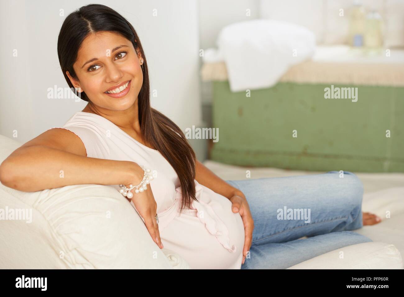 Smiling, pregnant woman sitting on chaise longue Stock Photo