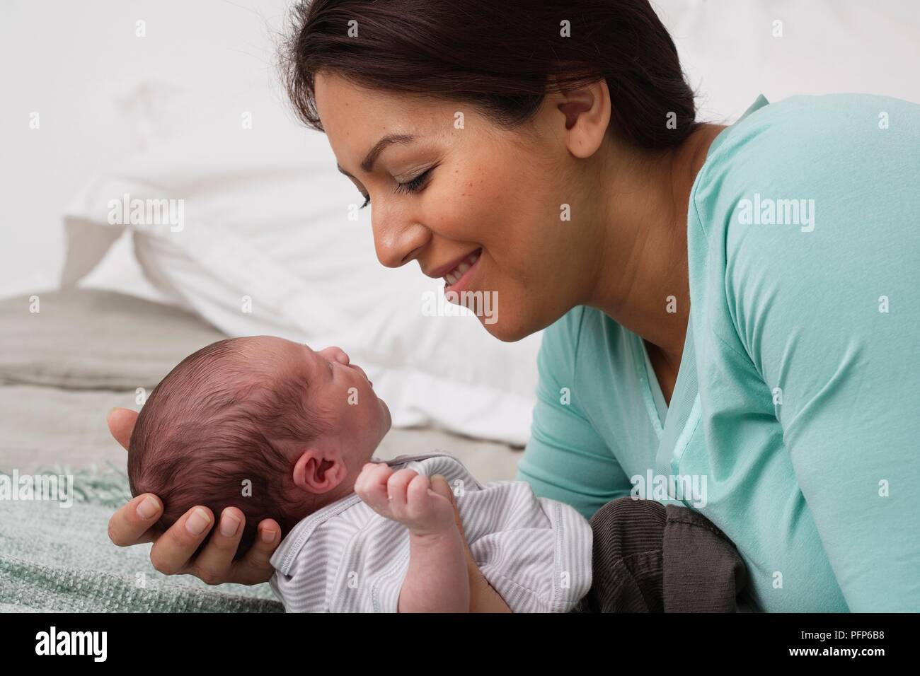Mother leaning over a baby boy, holding his head in her hands, side