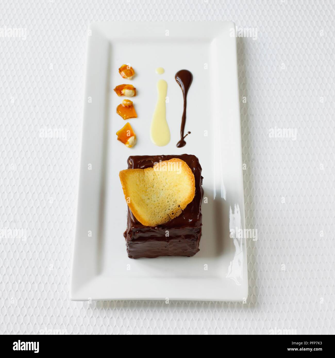 Chocolate and praline gateau with peanut brittle on rectangular white plate, close-up Stock Photo