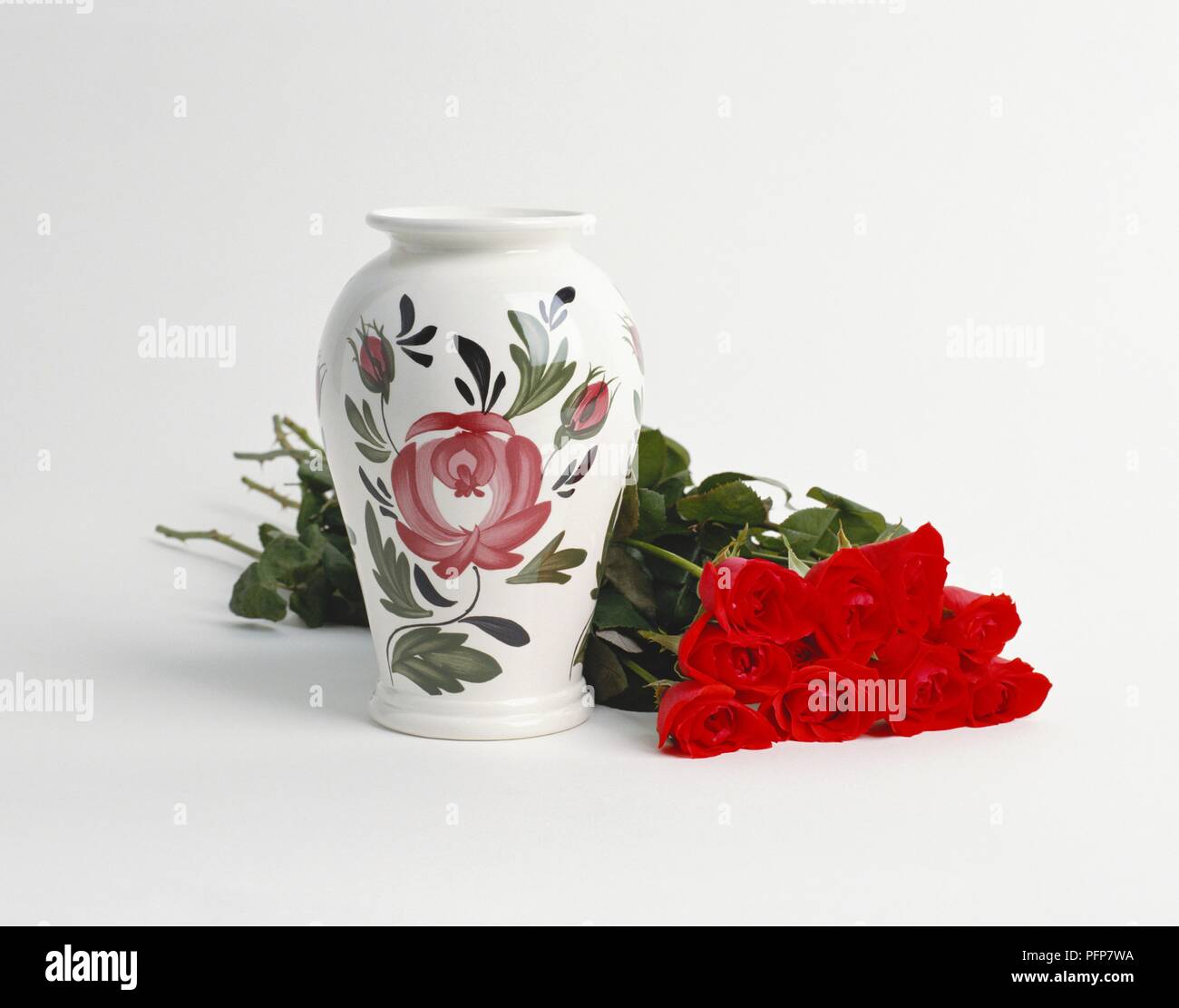 Bunch of red roses next to vase decorated with floral pattern Stock Photo