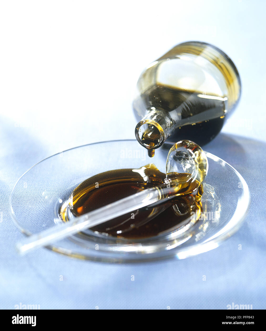 Pomegranate molasses dripping from glass bottle onto clear glass saucer, closeup Stock Photo