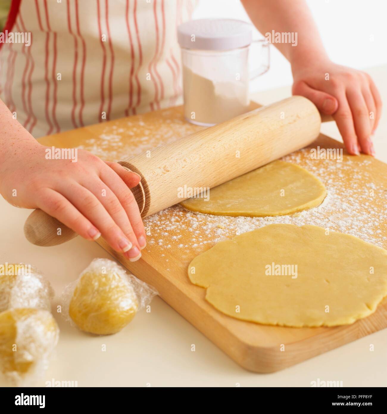 Girl using rolling pin on wooden chopping board to roll pastry balls