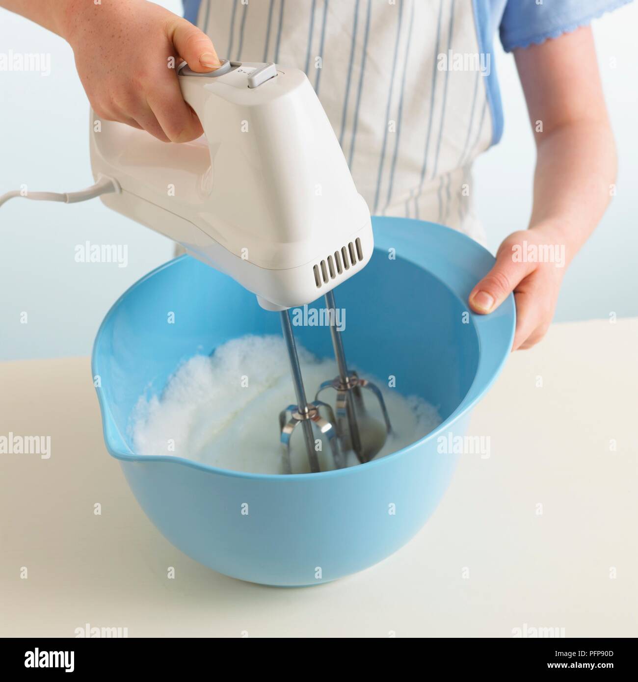 Girl using electric whisk to whisk egg whites in bowl