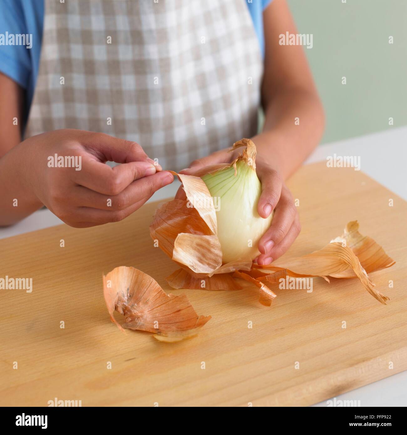 Girl peeling onion on chopping board Stock Photo